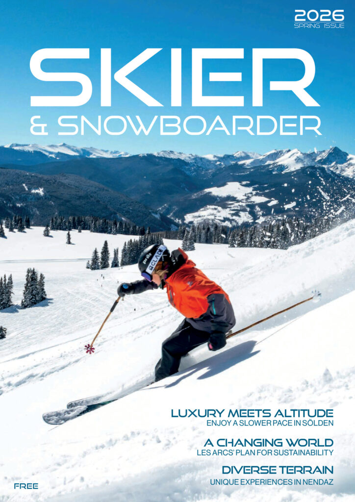 Cover of the Spring 2026 Skier & Snowboarder: a skier in an orange jacket carving through fresh snow below a blue sky and mountain ridge.
