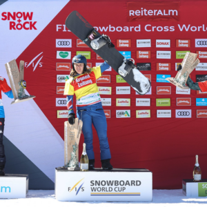 There’s no catching Bankes in race for Snowboard Cross Crystal Globe Three snowboarders stand on a podium at the Reiteralm FIS Snowboard Cross World Cup, holding trophies and their boards.