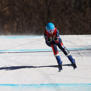 Paralympics Beijing 2022: Golden Simpson brothers pick up another medal in the Super Combined A skier in a blue helmet and GB racing suit crouches in an aerodynamic tuck on a snowy course marked with blue lines.