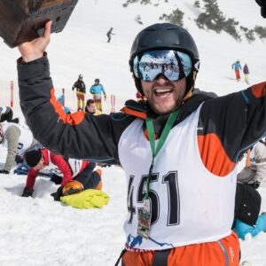 Brand new car is one of the buried treasures waiting to be dug up on the piste Smiling man in helmet, goggles and race bib 151 raises a wooden trophy on a snowy slope surrounded by other competitors.
