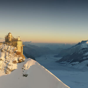 Spring skiing in the Jungfrau region until May 1 A domed mountain building perched on a snowy ridge, overlooking a vast glacier valley and distant peaks bathed in golden light.