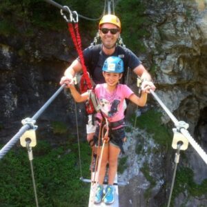 Whether you want to relax or get active, the French mountains have something for everyone this summer A man and young girl in safety helmets and climbing harnesses cross a cable suspension bridge above a rocky gorge with a waterfall below.