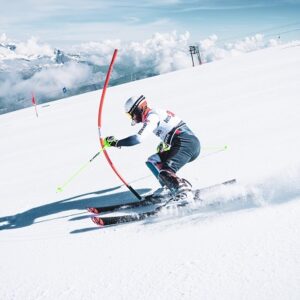 Early summer season start for skiers and snowboarders on Les 2 Alpes glacier A skier in racing gear carves around a red slalom gate on a snowy alpine slope with clouds and peaks behind.