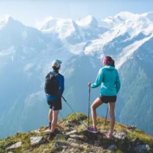 New signs put cycling on the map in Chamonix Valley Two hikers with backpacks and poles stand on a grassy ridge, gazing across a hazy range of snow-capped mountains.
