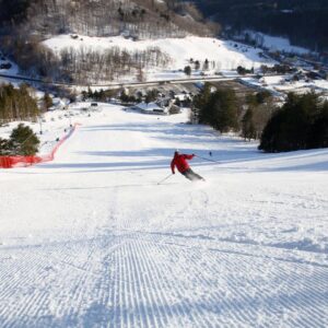 'Growing concerns' surrounding mental health prompts historic ski area to change its name A skier in a red jacket carves down a freshly groomed slope, with a red safety net, ski lift, village and forested mountains in the background.