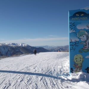 Ski and snowboard areas in Andorra unite under one pass covering more than 300km of piste Snowy ski slope with a distant skier and a blue 'MON(T) MAGIC' sign featuring cartoon characters.