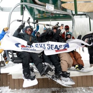First chair celebrates official opening of Colorado Ski Country USA ski season A group of snowboarders sits on a chairlift holding a "Colorado Ski Season" banner at a snowy resort.