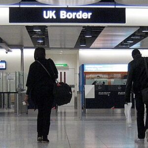 Airports make plans to minimise disruption during Border Force strike action over festive holidays Two travellers with luggage walk through the UK Border arrivals hall past automated gates under an overhead sign.