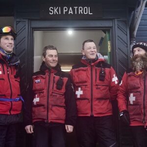 International Ski Patrol Day honours those who help keep skiers and snowboarders safe on the slopes Four men in red ski patrol uniforms stand smiling together outside a wooden building with a "SKI PATROL" sign above the door.
