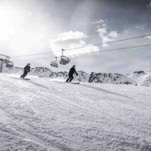 Gurgl gears up for this season Two skiers descend a sunlit snow slope beneath a chairlift, with rugged mountains rising in the background.