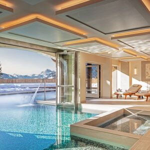Four Seasons Megève offers once in a lifetime experience to skiers and snowboarders Indoor pool and hot tub with wooden loungers open through large glass doors to a view of snow-covered mountains.