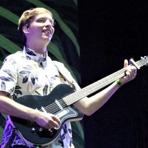 George Ezra to perform at Top of the Mountain Spring Concert in Ischgl A blonde musician in a leaf-patterned shirt plays a black electric guitar on a dimly lit stage.