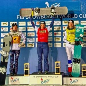 Sierra Nevada victory moves Bankes into top spot in Snowboard Cross World Cup standingss Three snowboarders stand on a podium at the FIS Snowboard World Cup in Cortina; the centre winner raises a board overhead.