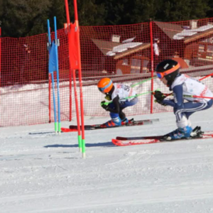 English Alpine Championships serves up another nine days of thrills and spills in Bormio Two skiers in racing tuck positions navigate red and blue slalom gates on a snowy course, with orange safety netting and a wooden building behind.