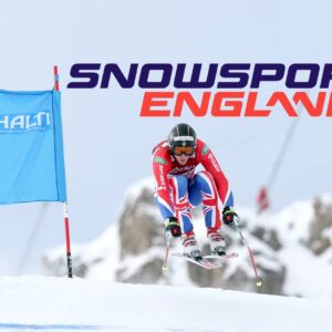 Halti and Snowsport England team up in new partnership Skier in a Union Jack racing suit tucks past a blue Halti gate banner beneath a Snowsport England logo against a misty mountain backdrop.