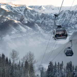 Telluride celebrates its 50th anniversary and announces events for 23/24 season Two Telluride gondolas ascend above snow-dusted pine trees toward a vast, misty mountain range.