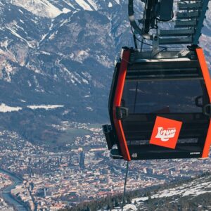Upgrades and ease of access makes Axamer Lizum ideal for a ski city break A red and black Leitner cable car numbered 48 hangs over an Alpine town with snow-dusted mountains in the background.