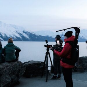 Ski film featuring all-female cast hits the silver screen in London on 30 May A film crew with cameras and a tripod photograph a couple sitting on rocks, looking out at snow-capped mountains across the water.
