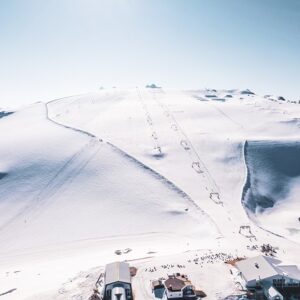Three French resorts announce plans to open glaciers for skiing and snowboarding during the summer Wide snow-covered mountain with ski tracks winding down the slope, tiny skiers descending towards buildings clustered at the base.
