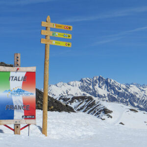 Win a family skiing holiday to Italy! Snow-covered signpost and Italie/France border marker for La Rosière-San Bernardo at 2575m, set against mountain peaks.