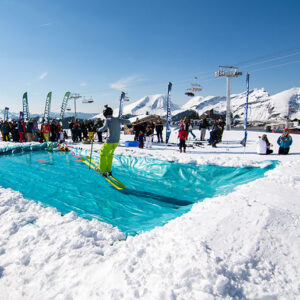 Celebrate the end of the winter season in Avoriaz A skier in yellow trousers glides across a bright turquoise pool of water cut into the snow, watched by a crowd beneath snow-capped mountains and chairlifts.