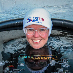 Smiling woman in a white DSUK Disability Snowsport UK beanie and Billabong wetsuit submerged in an ice bath.