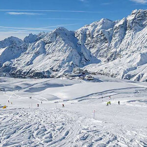 Travel agency reveal their top 6 Italian resorts for this spring Skiers descend wide snow-covered slopes beneath jagged, snow-capped peaks under a clear blue sky.