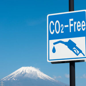 Carbon Neutral Airport Ski Transfers A blue and white "CO2-Free" sign featuring a fuel pump icon stands against a clear sky, with a snow-capped mountain in the background.