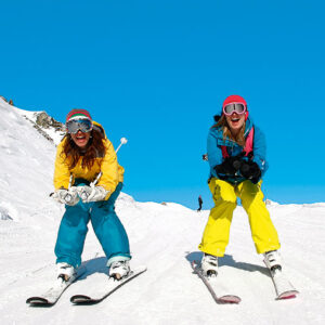 Action Outdoors launches expanded programme of holidays for young people Two skiers pose on a snowy slope in colourful gear under a bright blue sky.