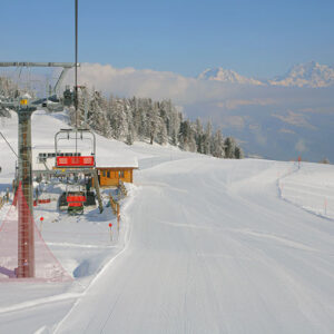 Win a ski holiday for 4 people to Pila worth over £1,600 Red chairlift station and wooden hut on a snow-covered piste, with snow-laden evergreens and distant mountain peaks under a clear blue sky.