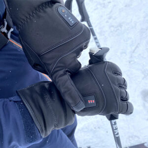 Black leather ski gloves with illuminated LED indicators grip ski poles against a snowy backdrop.