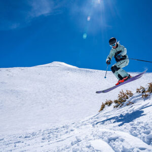 Early openings as snow falls at Vail Resorts’ Northern Hemisphere resorts Skier in white suit and helmet launches off a snowy ridge under a bright blue sky.