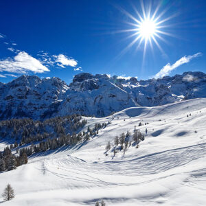 What’s new in Trentino this winter Snow-covered mountains with ski tracks crisscrossing the slopes, bathed in bright sunlight under a clear blue sky.