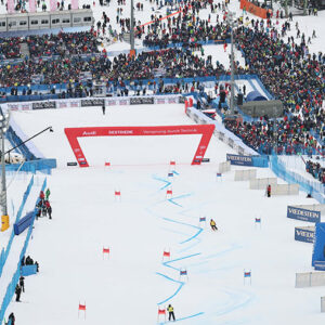 Skier makes history at Vialattea's Audi FIS Ski World Cup Crowds line a snowy ski race finish area beneath a red "Audi Sestriere" arch, with slalom gates descending the slope and "Vedesten" banners to the right.
