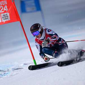 18 year old skier Molly Butler to get Evie Pinching Award Skier in racing kit carves sharply past a red Gangwon 2024 Youth Olympic Games gate on a snowy slope.