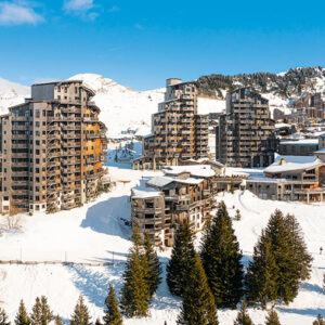 Exciting Updates for 2025/2026 Season at Premium Residences in France Cluster of tall wooden apartment blocks and chalets on a snow-covered mountain, with pine trees and skiers below.