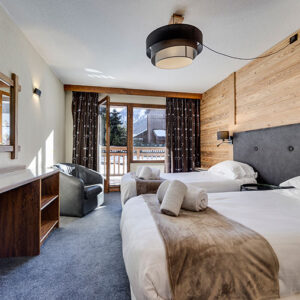 Neilson Expands Ski Offering in Val D'Isere with Two New Hotels Wooden alpine bedroom with twin beds, rolled towels, a desk and a balcony overlooking snow.