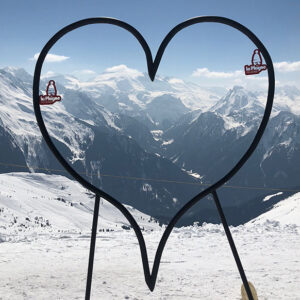 Self catering family holidays in La Plagne A large heart-shaped frame in the snow frames a panoramic view of the Alps, with two "la Plagne" penguin stickers attached to its sides.