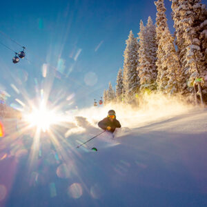 Colorado: 7 resorts offering something for every type of skier Skier carving through deep powder with sun flare, snow-laden evergreens and a ski lift visible in the background.