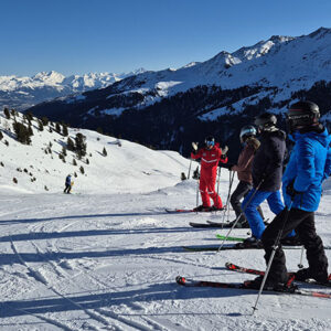 Head to Nendaz for diverse terrain and unique experiences A group of skiers stands on a snowy slope looking out across sunlit alpine mountains beneath a clear blue sky.