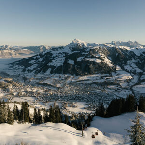 Kitzbühel: Where tradition and modern alpine lifestyle meet Snow-covered valley town nestled between alpine peaks, with a ski lift in the foreground and low cloud filling the valley floor.