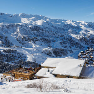 Méribel to host ‘dinner in the sky’ experience Snow-covered mountain landscape with a wooden chalet in the foreground and a village nestled in the valley below the ski slopes.