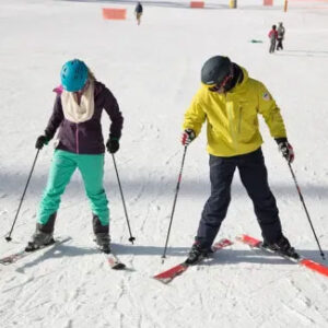 Train Off the Slopes: Sports That Make You a Stronger Skier and Snowboarder Two skiers in helmets and goggles, one in a purple jacket and teal trousers, the other in a yellow jacket, stand on a snowy slope holding their poles.