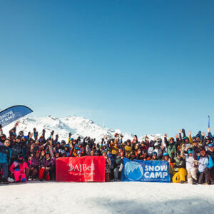 Snow Camp celebrates success of 2026 AJ Bell 3 Valley A large group of skiers and snowboarders pose on a snowy mountain with arms raised, alongside Snow Camp and AJBell banners.