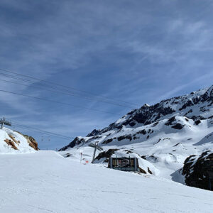 Agency reveals which French resorts 'have won this ski season' Snowy mountain ski slope with chairlift cables, a stone building, and rocky peaks under a blue sky streaked with wispy clouds.