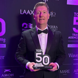 Iglu wins top ski/snowsports agency award A man in a black tuxedo and bow tie smiles while holding a "Top 50 2026 Travel Agencies" award in front of a purple sponsor backdrop.