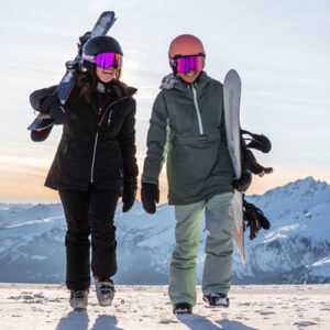 Ski Confidence Week launched to help skiers feel more in control on the slopes Two people in ski gear and goggles walk across snow carrying skis and a snowboard, with snow-capped mountains behind them.